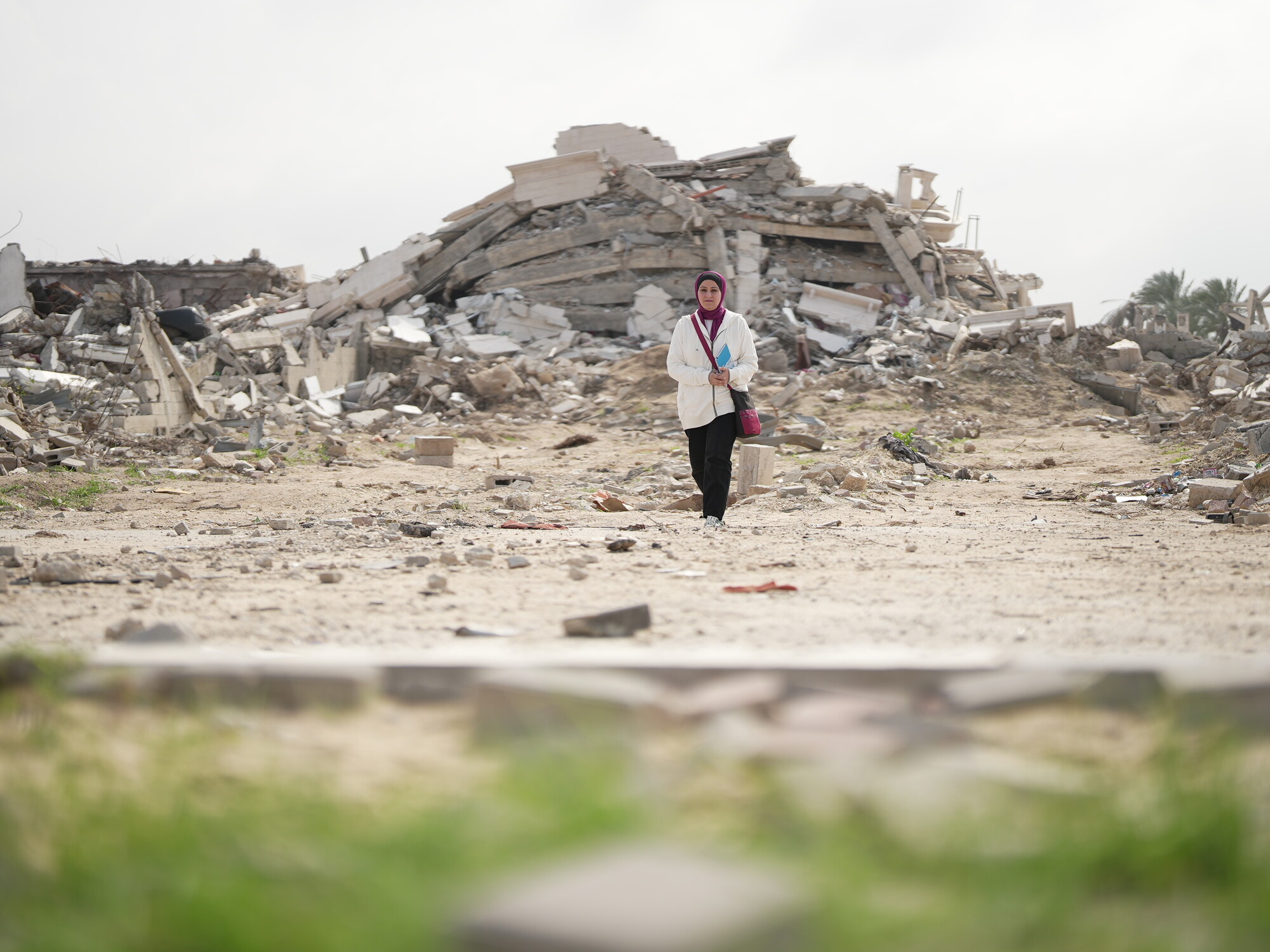 Gaza, Palestinian Territory, Occupied: Fidaa Shurrab, Director of Projects at Atfaluna for Deaf Society in Rafah stands in front of a destroyed building in Gaza strip while going to work. Photo: Alef Multimedia/Oxfam