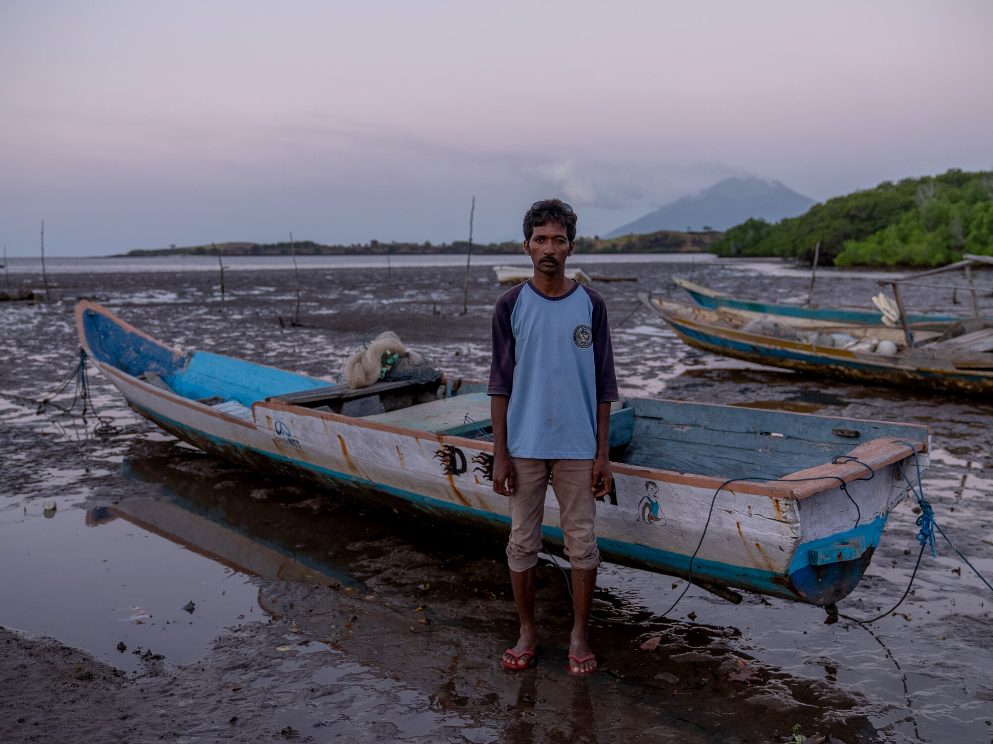 Mekko, Indonesia: Said (33) stands in front of his fishing boat. He now struggles to catch enough fish for his family's daily needs, due to climate change and the fish moving further and further out to sea. Photo: Vikram Sombu/Oxfam. Oxfam acknowledges the support of the Australian Government through the Australian NGO Cooperation Program (ANCP)