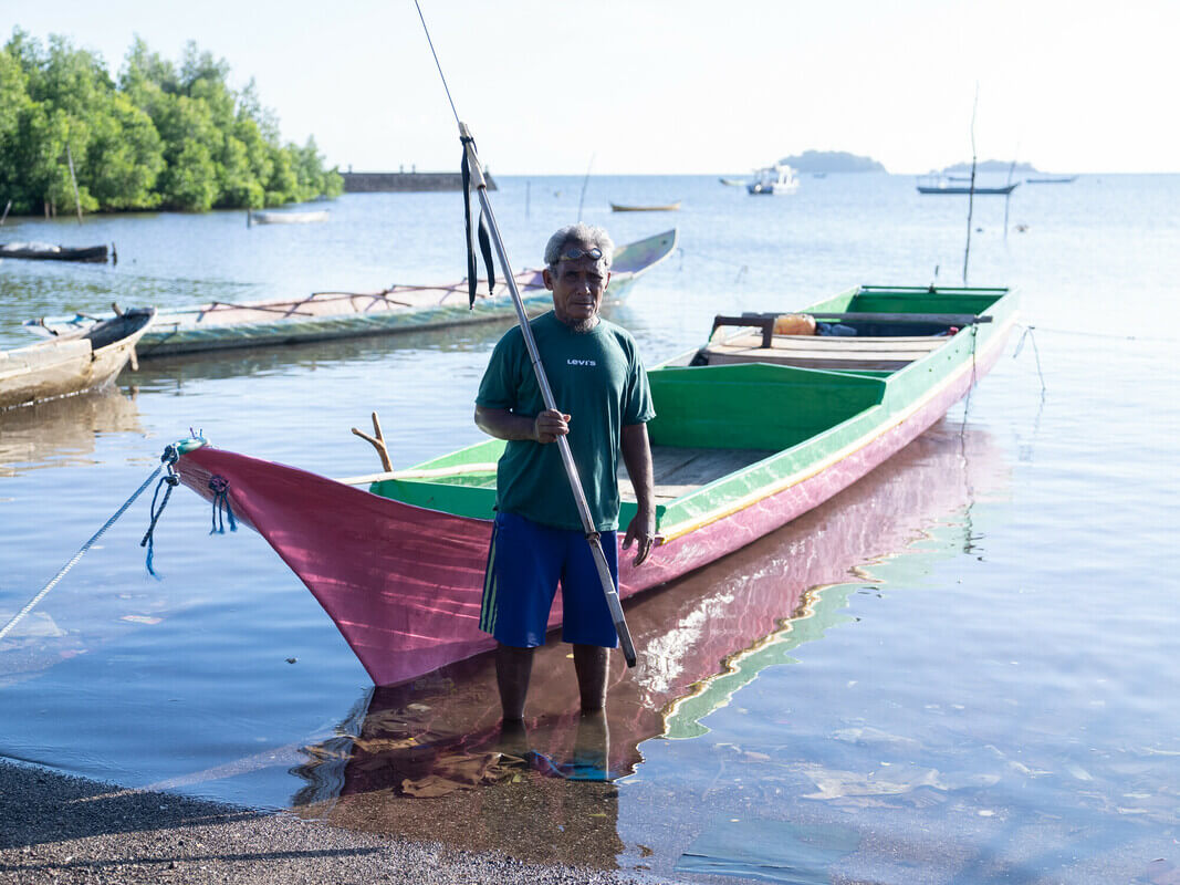 Mekko, Indonesia: Tasman (63) in front of the boat he uses for spear-fishing. He now struggles to catch enough fish to meet his daily needs as climate change has caused fish to move further and further out to sea. Oxfam acknowledges the support of the Australian Government through the Australian NGO Cooperation Program (ANCP). Photo: Vikram Sombu/Oxfam