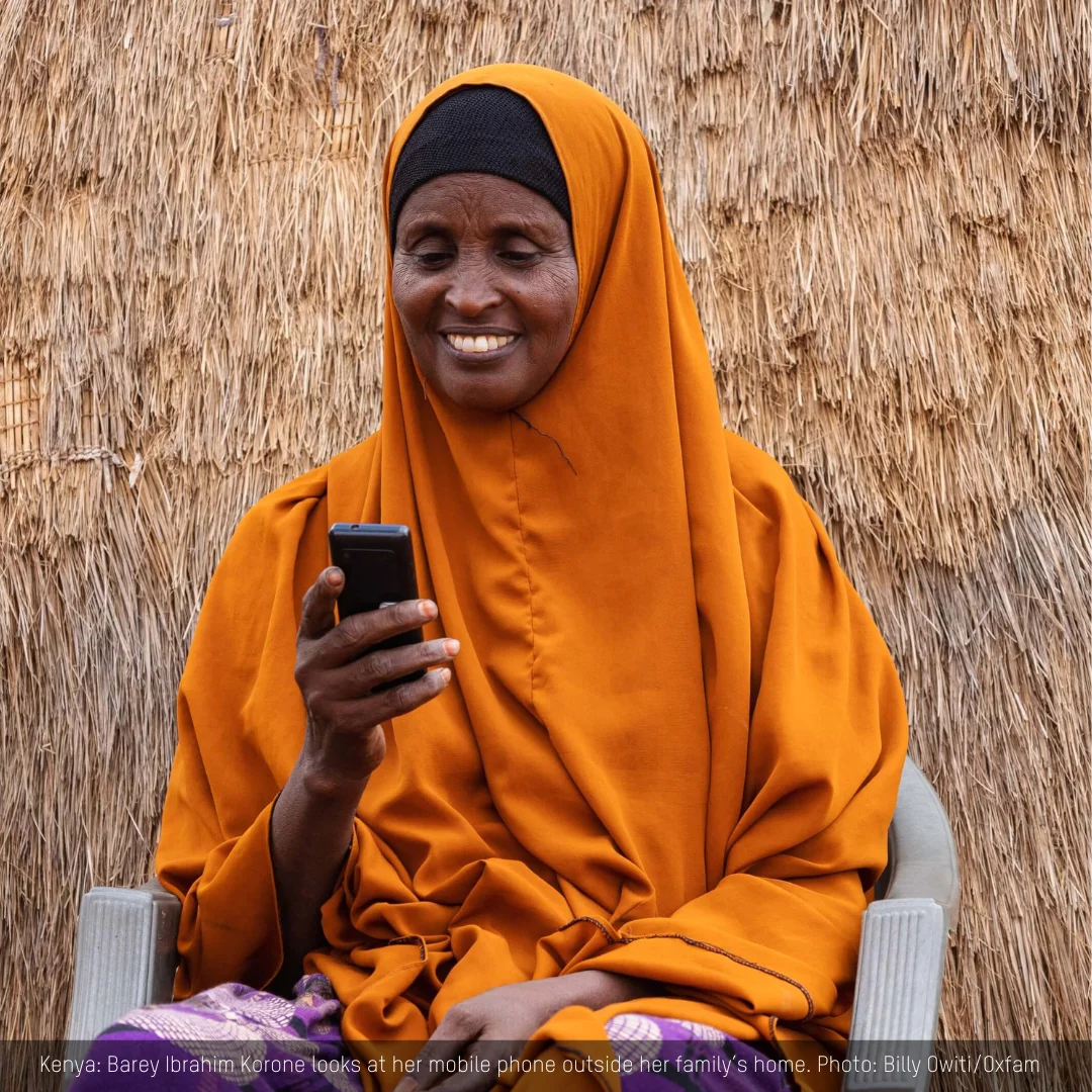 Kenya: Barey Ibrahim Korone is all smiles as she looks at her mobile phone outside her family hut in Tula Tula, Wajir. Billy Owiti/Oxfam