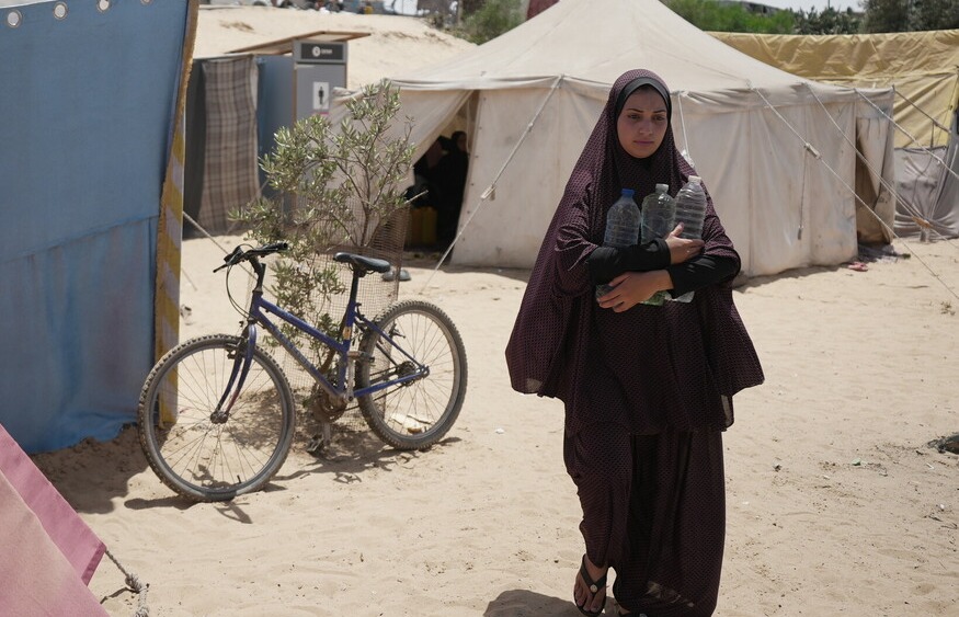 Palestinian Territory, Occupied: Duaa Abu Sabha holds water bottles while walking to her tent in the Al-Mawasi area in Khan Yunis Governorate. Photo: Alef Multimedia/Oxfam.